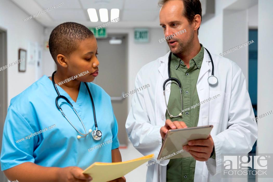 Stock Photo: Couple of diverse male and female doctors walking through corridor looking at tablet.
