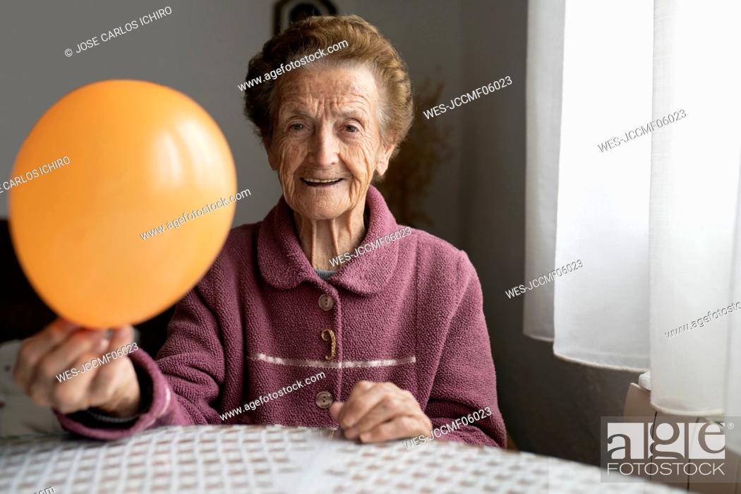 Stock Photo: Smiling woman with orange balloon sitting at dining table.