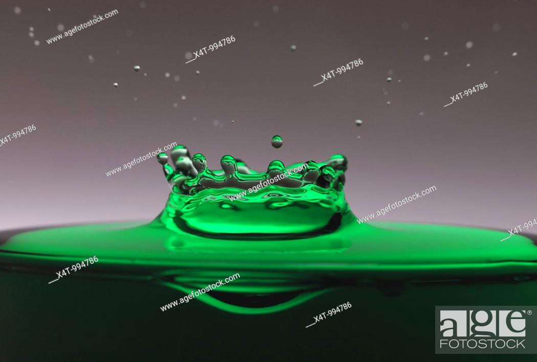 Stock Photo: A drop of green water forming a coronet as it splashes into a glass full of liquid, backlit for contrast.