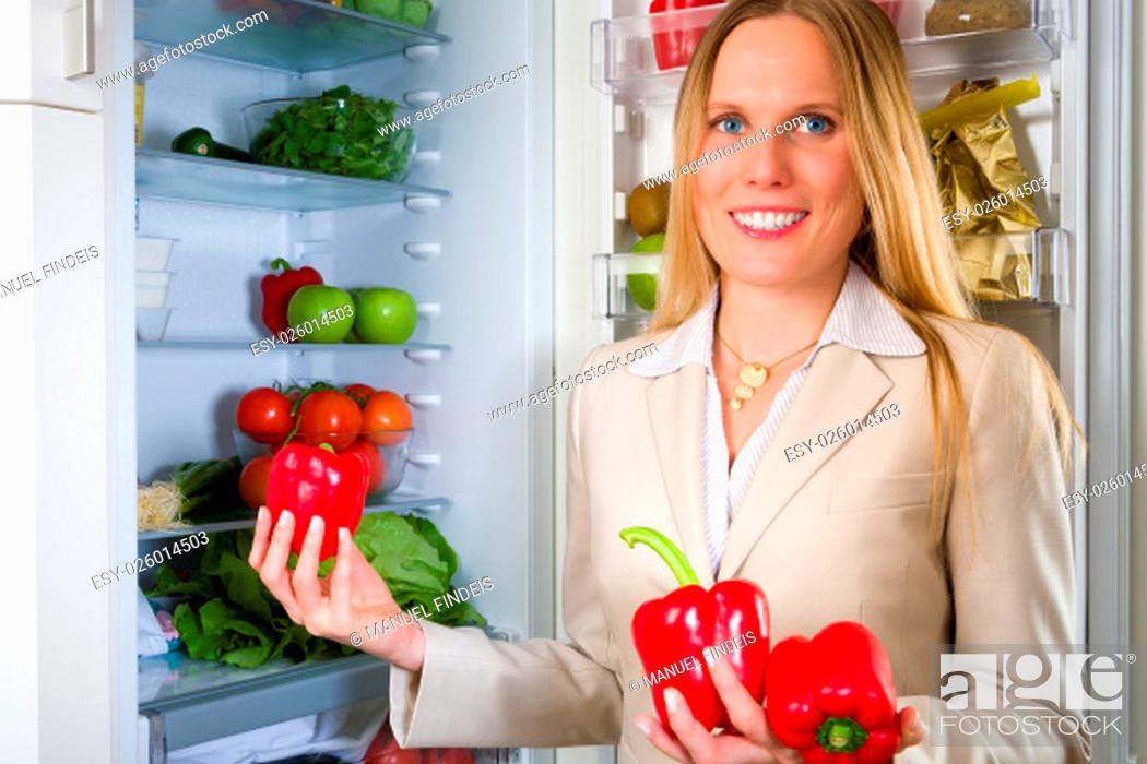 Stock Photo: Attractive business woman showing vegetables for healthy eating in front of a refrigerator.