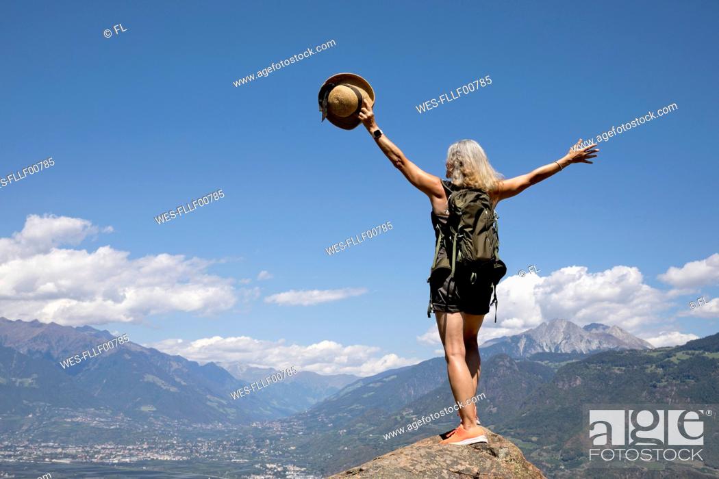 Stock Photo: Carefree senior woman with arms raised standing on rock in front of mountains.