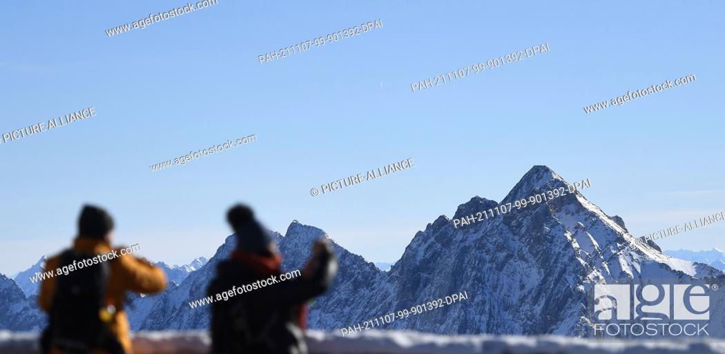 Stock Photo: 07 November 2021, Bavaria, Grainau: Two visitors photograph the panorama of the Wetterstein mountains from the Zugspitze. Photo: Angelika Warmuth/dpa.