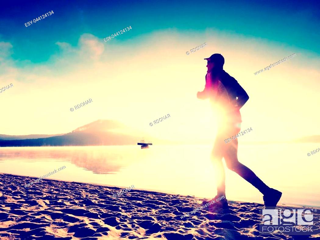 Stock Photo: Silhouette of sport active man running on the lake beach at sunrise. Healthy lifestyle. Alone young fitness man exercise at morning beach.