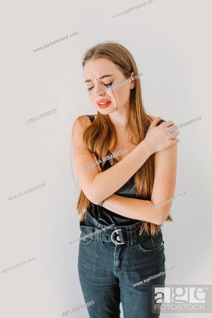 Stock Photo: Depressed woman with hand on shoulder crying in front of wall.