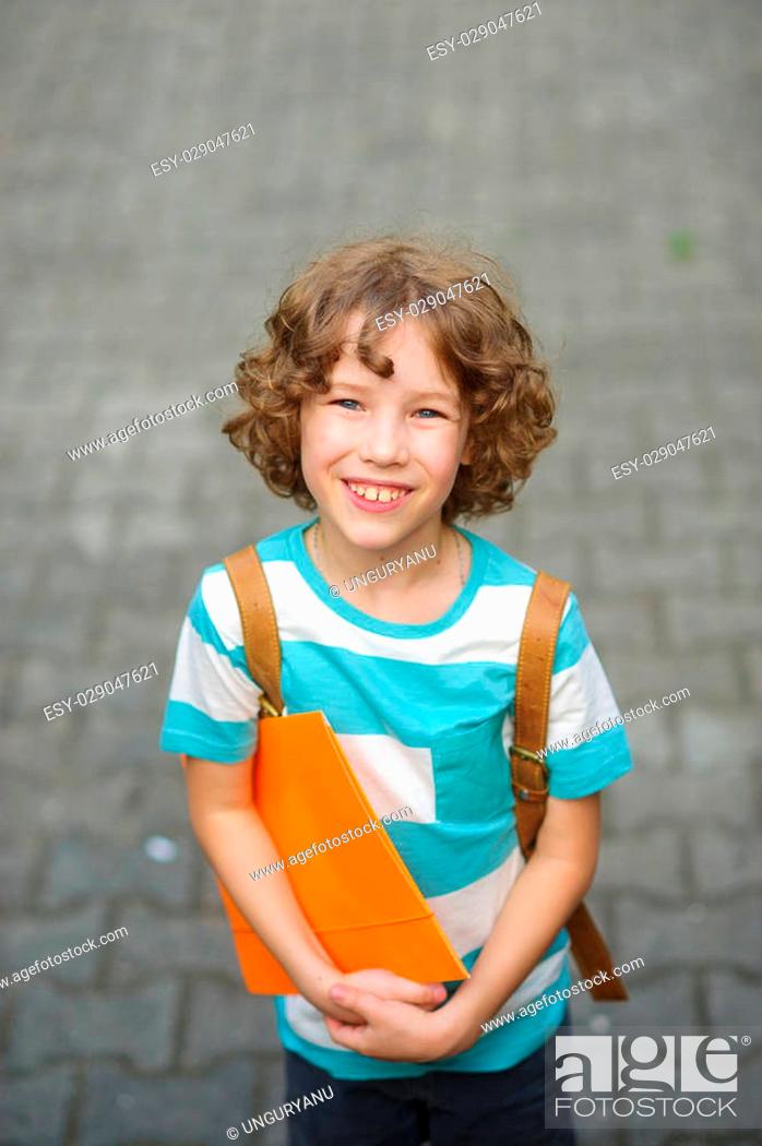 Photo de stock: The fair-haired curly schoolboy looks in the camera and smiles. The boy has a nice face, a fair hair, an open look. It has behind shoulders a satchel.