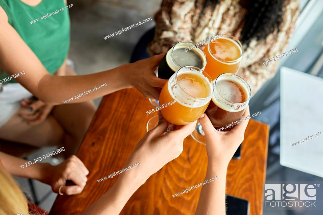 Stock Photo: Female friends clinking craft beer glasses in a pub.