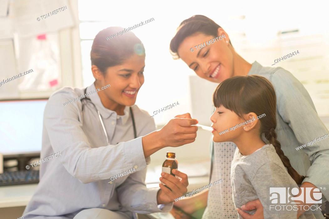 Stock Photo: Female pediatrician feeding cough syrup to girl patient in examination room.