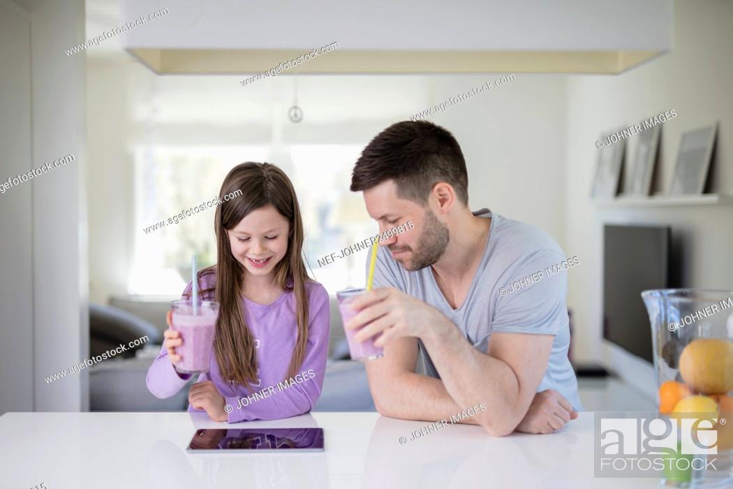 Stock Photo: Father and daughter having smoothies while looking at digital table.