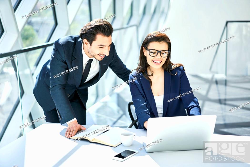 Stock Photo: Smiling businesswoman and businessman using laptop at desk in modern office.