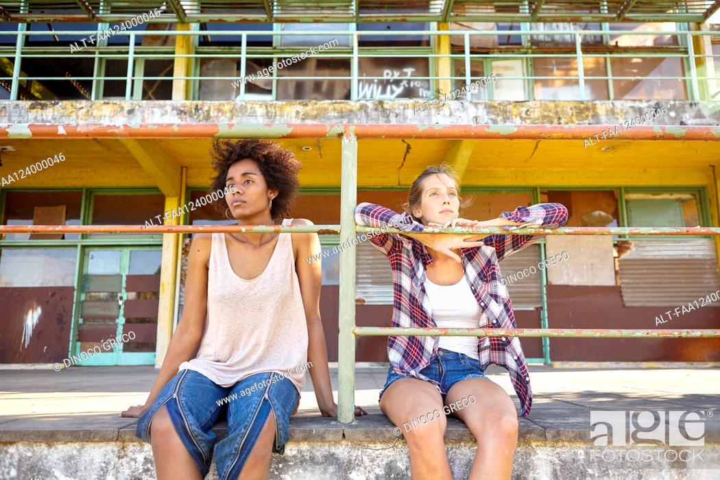 Photo de stock: Young female friends sitting near railings outdoors.