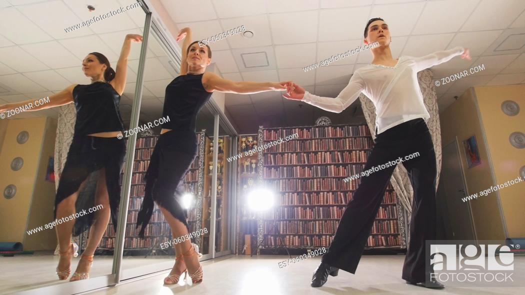 Stock Photo: Young attractive man and woman dancing and rehearsing Latin American dance in costumes in the Studio, focus reflection in the mirroron and legs.