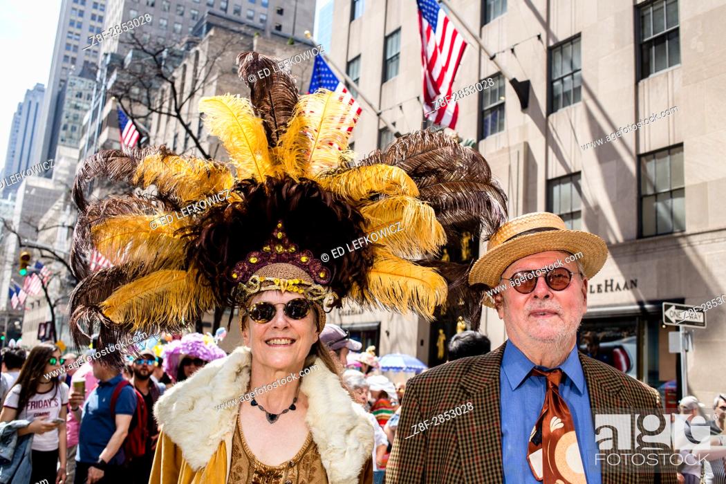 Stock Photo: New York, NY - April 16, 2017. A couple at New York's annual Easter Bonnet Parade and Festival on Fifth Avenue. She is wearing an elaborate hat with yellow and.