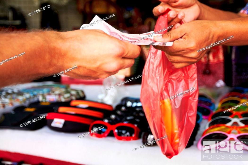 Stock Photo: Closeup of money exchanging hands at a market after buying a pair of sunglasses.