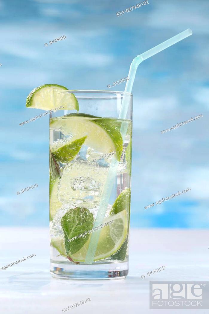 Stock Photo: Glass of sparkling water with ice cubes garnished with a slice of lime and mint on blue sky background.