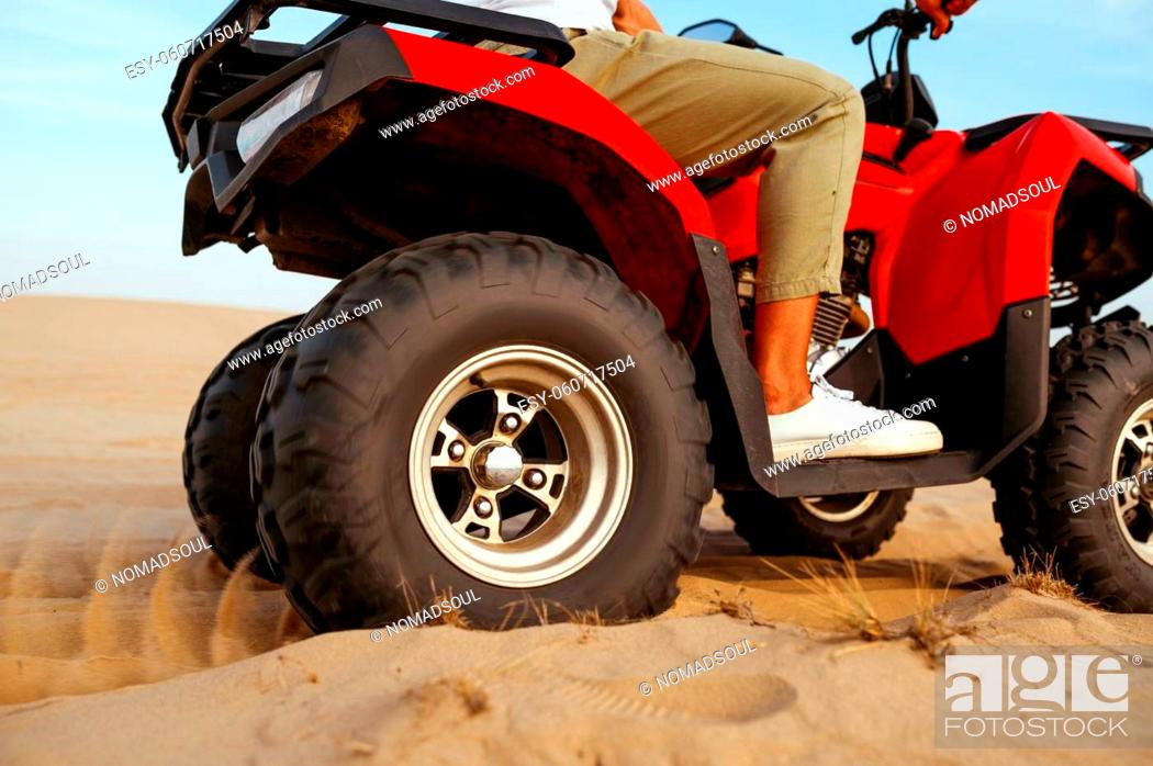 Stock Photo: Man in helmet rides on atv, downhill riding in desert sands, action view. Male person on quad bike, sandy race, dune safari in hot sunny day.