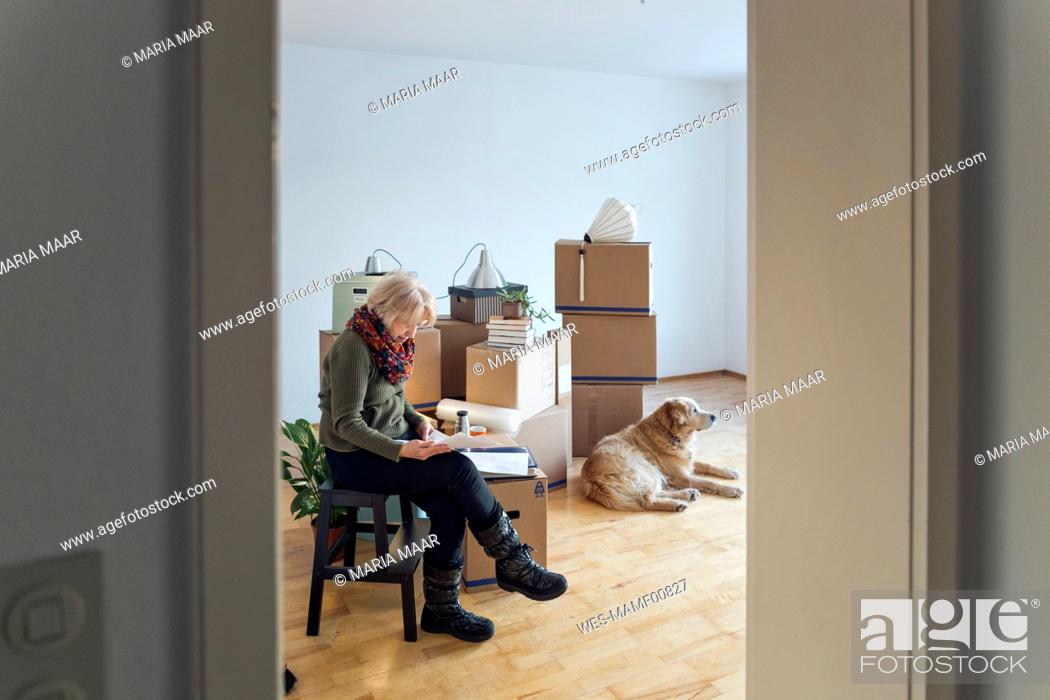 Stock Photo: Senior woman looking at papers surrounded by cardboard boxes in an empty room.