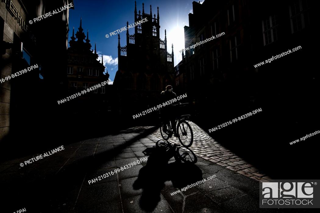 Stock Photo: ATTENTION: EMBARGOED FOR PUBLICATION UNTIL 16 MARCH 12:00 GMT! - 16 March 2021, North Rhine-Westphalia, Münster: A woman rides her bicycle on Prinzipalmarkt and.