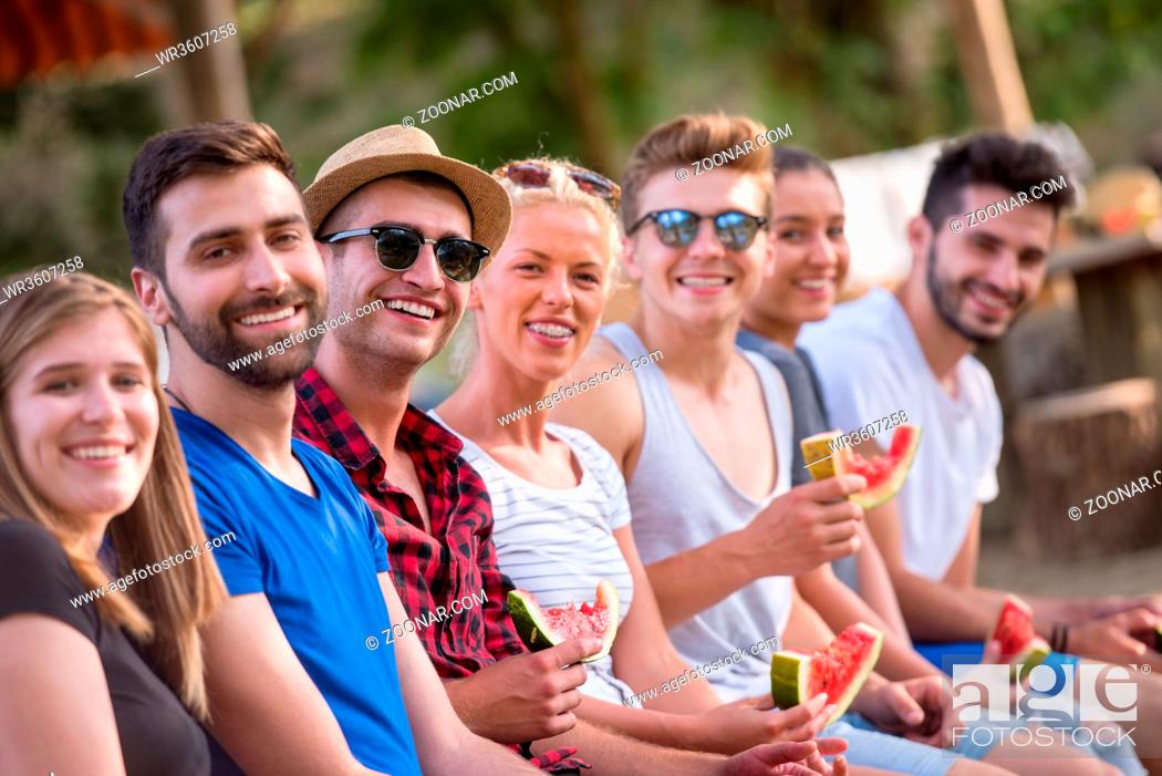 Stock Photo: group of young friends enjoying watermelon while sitting on the wooden bridge over the river in beautiful nature.