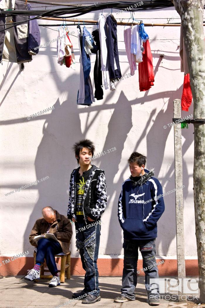 Stock Photo: Teenagers stand by a man sleeping in Zi Zhong Road, old French Concession Quarter in Shanghai, China.