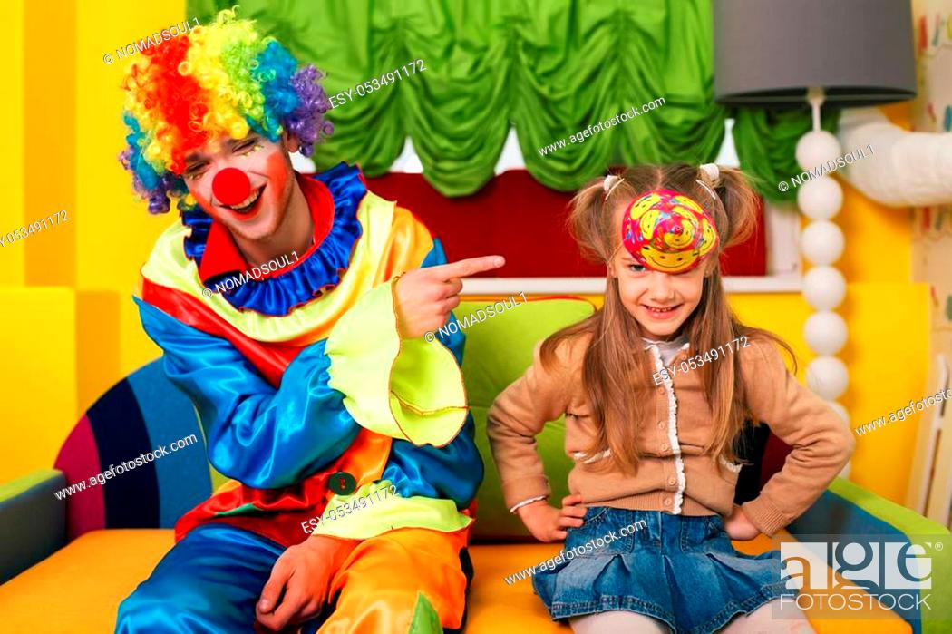 Stock Photo: Little girl has put on a cap, and the clown laughs at her. Kindergarten on the background.