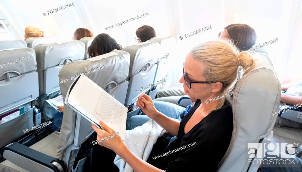 Stock Photo: Female traveler reading magazine on airplane during flight. Female traveler reading seated in passanger cabin.