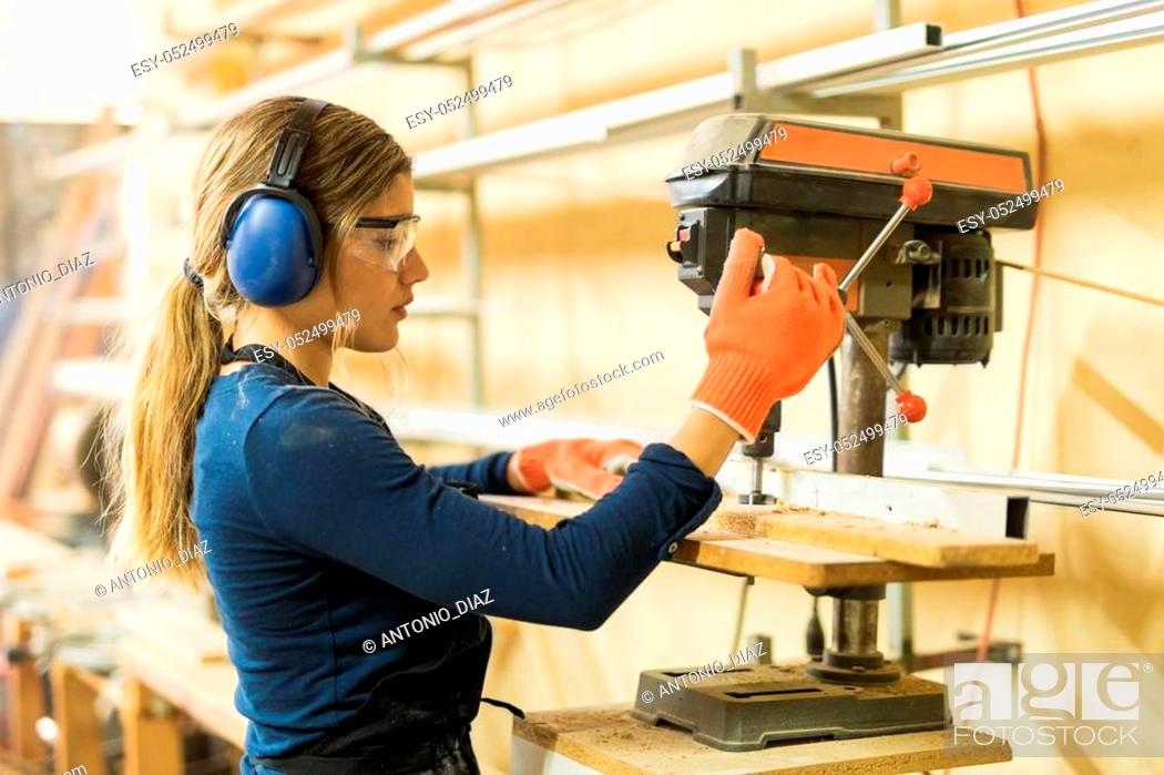 Stock Photo: Profile view of a young female carpenter using a drill press on a wood board in a woodshop.