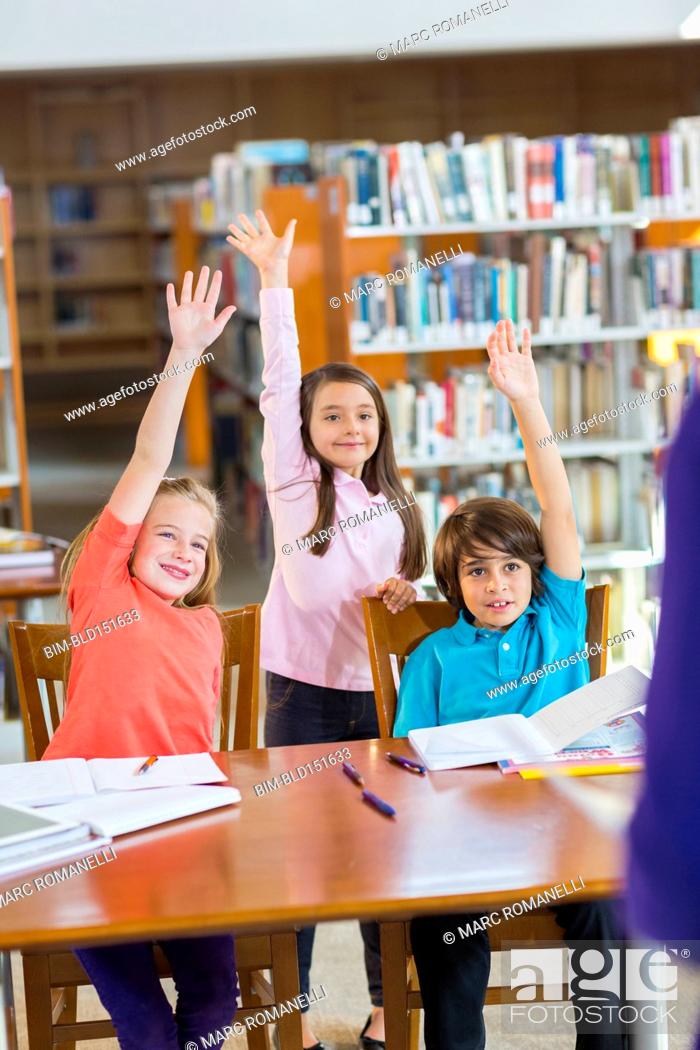 Stock Photo: Students raising their hands in library.