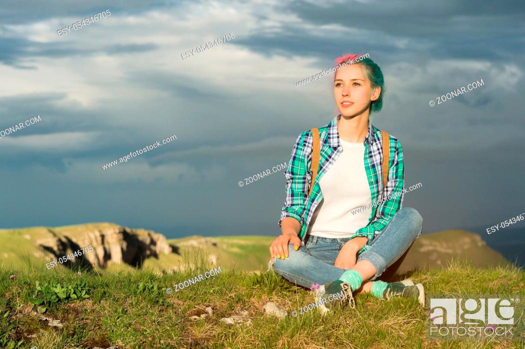 Stock Photo: Portrait of young smiling woman traveler with multi-colored hair. Sitting high in the mountains in the evening with a decline in the background of a plateau.