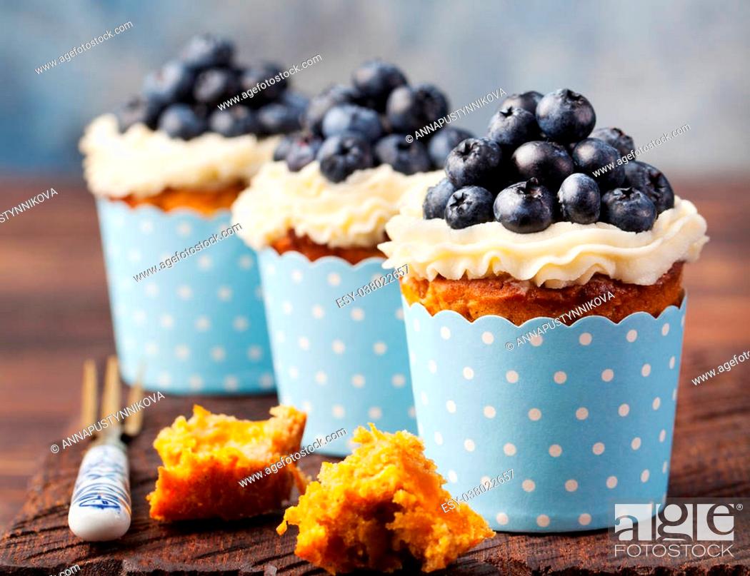 Stock Photo: Pumpkin cupcakes decorated with cream cheese frosting and fresh blueberries on a wooden background Copy space.