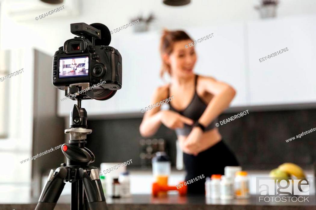 Stock Photo: Happy healthy young girl recording her video blog episode about healthy food additives while standing at the kitchen at home and showing smart watch.
