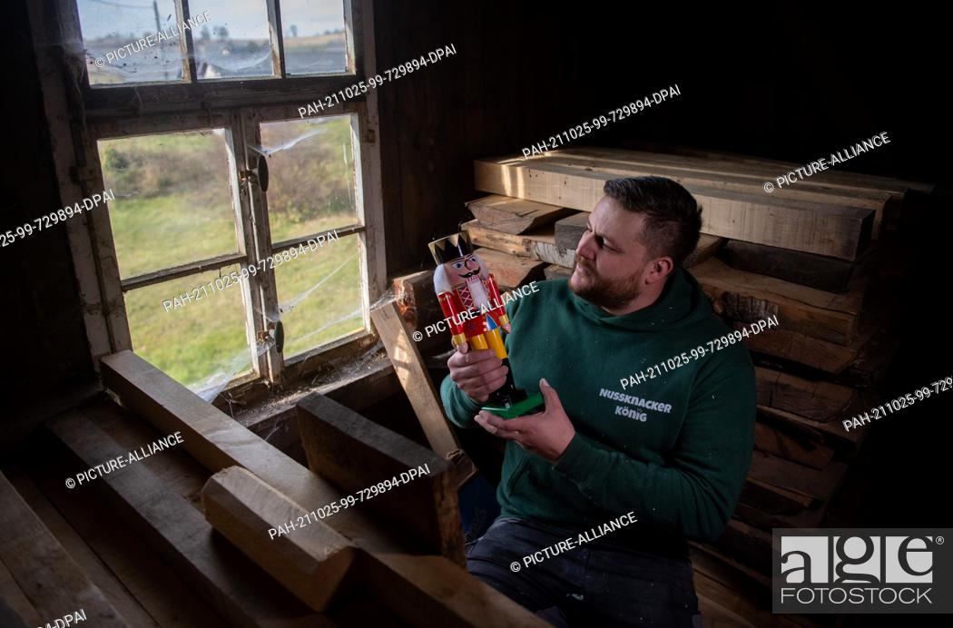 Stock Photo: 25 October 2021, Saxony, Seiffen: Wooden toy maker Markus Füchtner sits with a copy of the ""Red King"" in the wooden warehouse of his workshop in Seiffen.