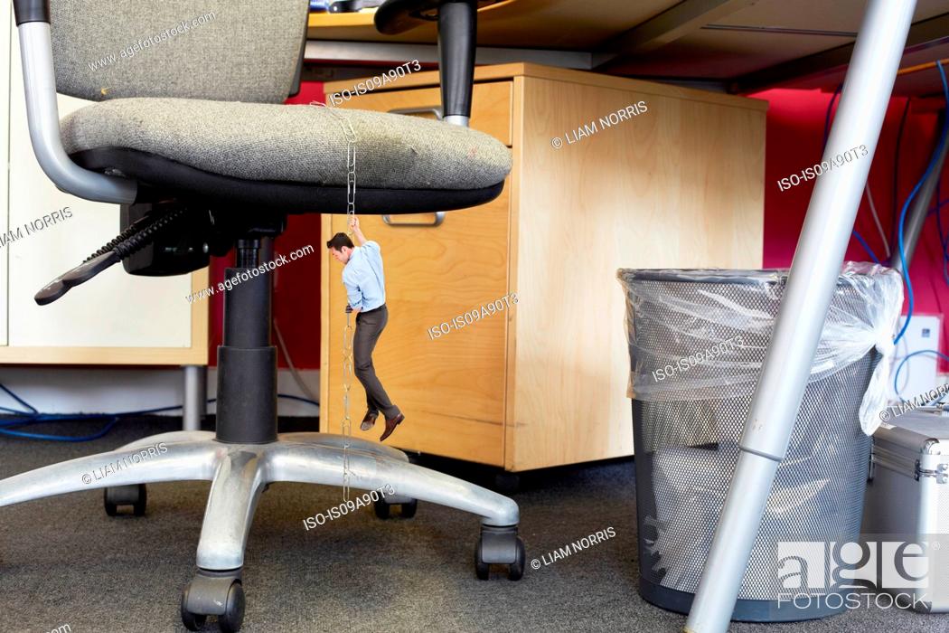 Businessman Climbing Down Large Paper Clips On Oversized Office
