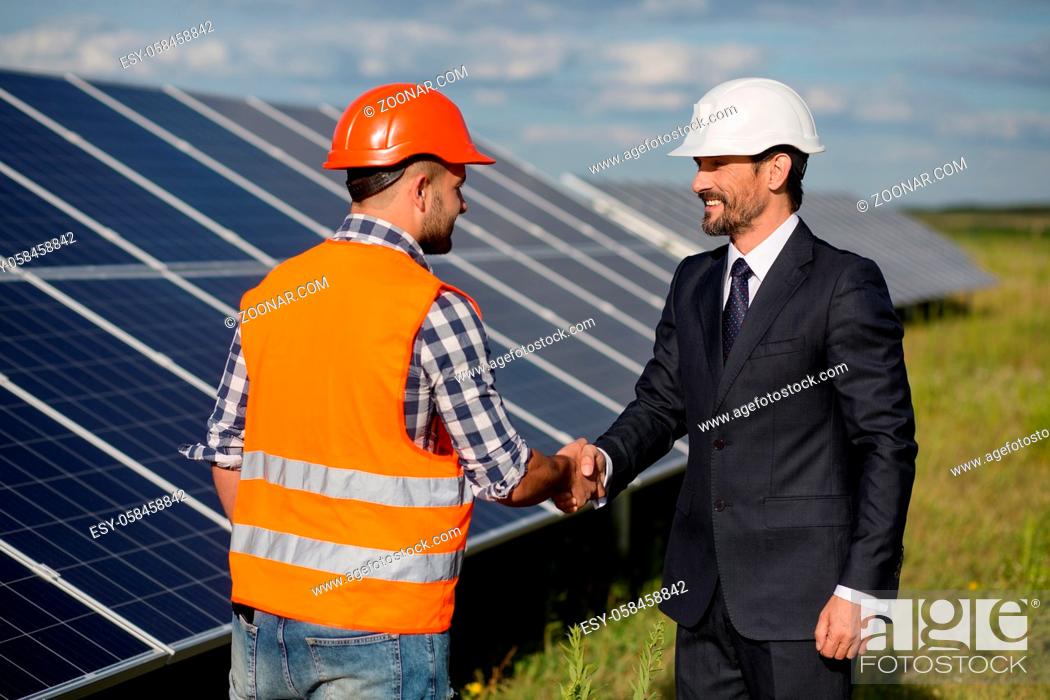 Stock Photo: Businessman and foreman shaking hands at solar energy station. Solar panels in the field, two men making agreement.