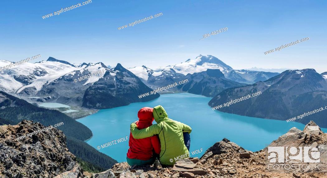 Stock Photo: View from Panorama Ridge trail, Two hikers sitting on a rock with Garibaldi Lake, turquoise glacial lake, Guard Mountain and Deception Peak, back glacier.