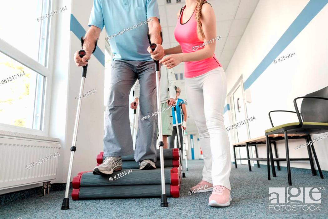 Photo de stock: Seniors in rehabilitation learning how to walk with crutches after having had an injury.
