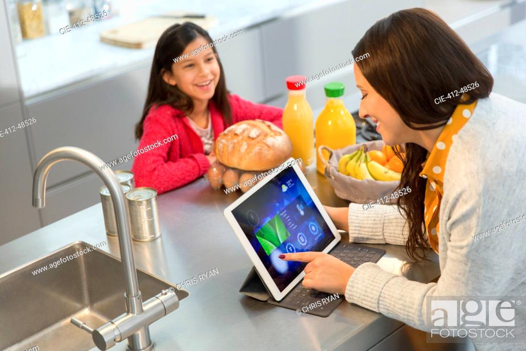 Stock Photo: Daughter watching mother using digital tablet in kitchen.