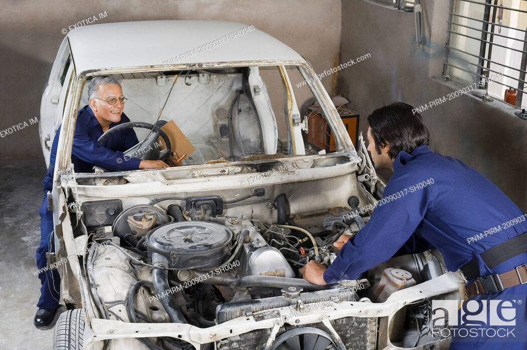Stock Photo: Auto mechanic with an apprentice repairing a car in a garage.