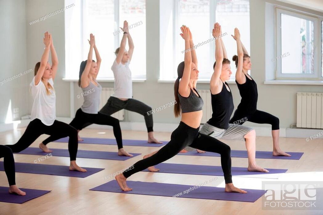 Stock Photo: Group of young sporty people practicing yoga lesson, doing Warrior one exercise, Virabhadrasana I pose, working out, indoor, students training in club, studio.