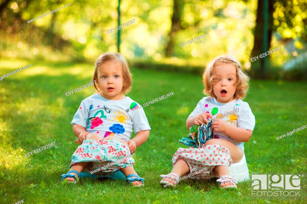 Stock Photo: The two little baby girls two-year old sitting on pots against green grass.
