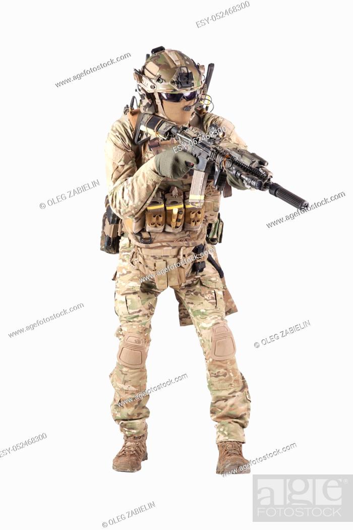 Stock Photo: Army infantryman in camouflage uniform, battle helmet, tactical radio headset, extra ammo on load carrier, sneaking, aiming with laser sight on assault rifle.