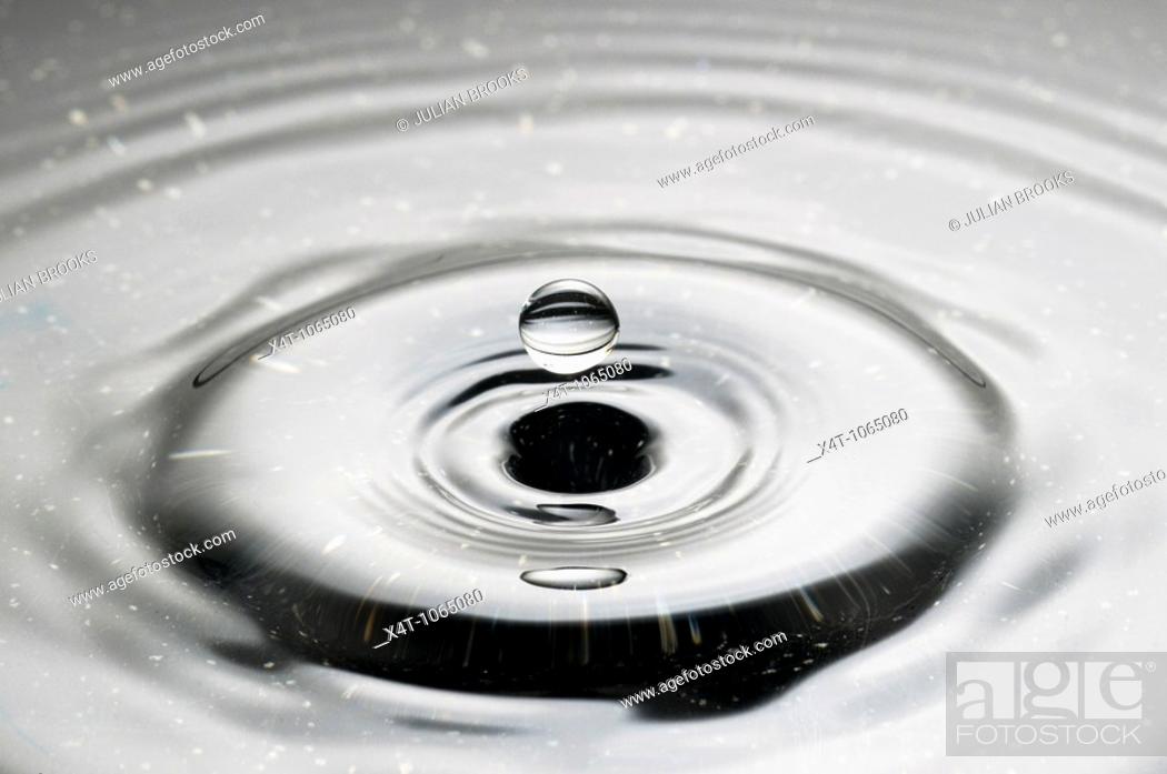 Stock Photo: A droplet of water falling into a puddle and creating ripples.