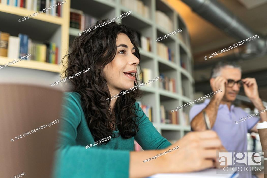 Stock Photo: Smiling businesswoman sitting in front of bookshelf.