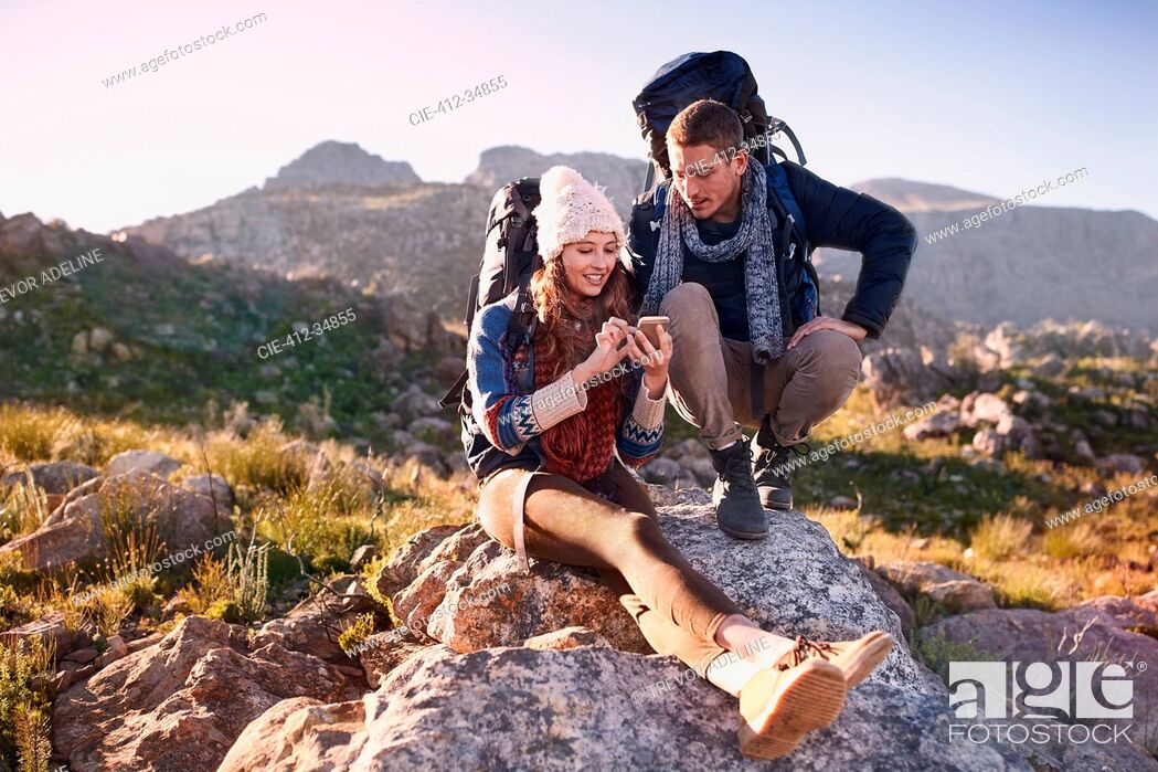 Stock Photo: Young couple with backpacks hiking, resting on rock using smart phone.