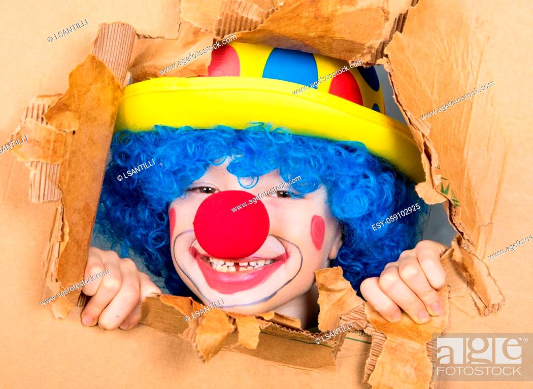 Stock Photo: young child dressed as a clown with wig and fake nose has fun watching from the open cardboard.