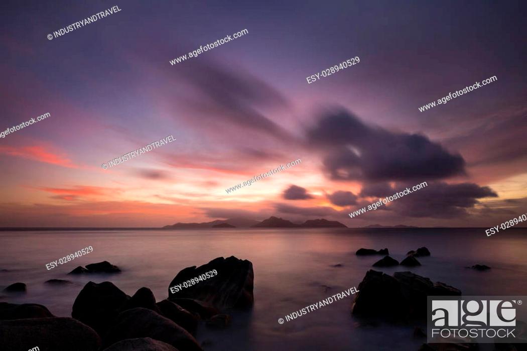 Stock Photo: Colorful sunset long exposure with view to Praslin from La Digue, Seychelles with granite rocks in the foreground.