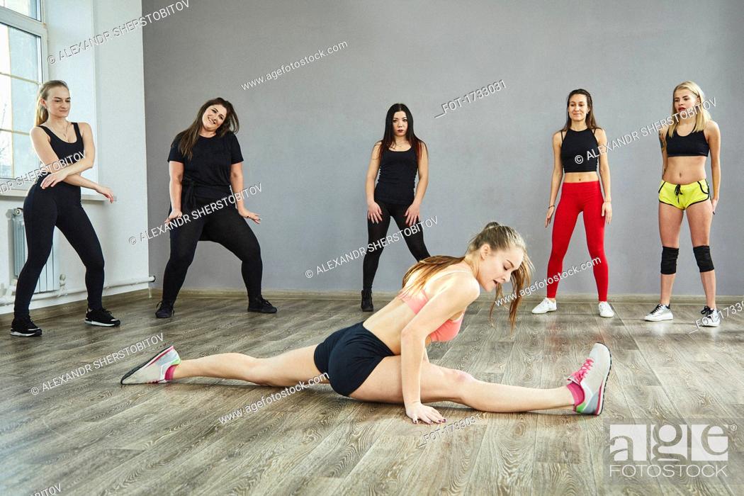 Stock Photo: Friends looking at young woman doing splits at dance studio.