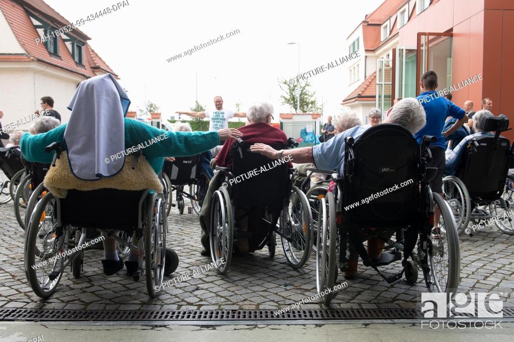 Stock Photo: 24 May 2018, Germany, Dresden: Residents effected by the evacuation in Dresden sitting during morning gymanstics at the site of the Dresden messe in an.