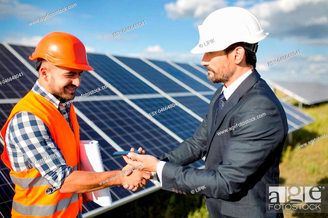 Stock Photo: Businessman holding photovoltaic detail and shaking hand to a foreman. Solar panels in the field, business deal between client and foreman.