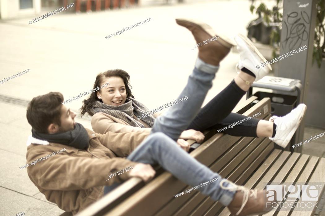 Stock Photo: young teenage couple sitting on bench the wrong way round in city, hanging out together, legs up, upside down, in Cottbus, Brandenburg, Germany.