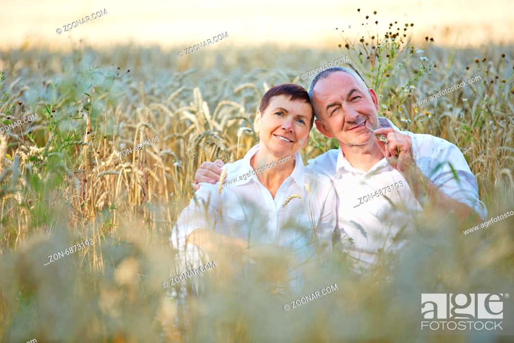 Stock Photo: Glückliches Paar Senioren sitzt in einem Feld voller Weizen im Sommer.